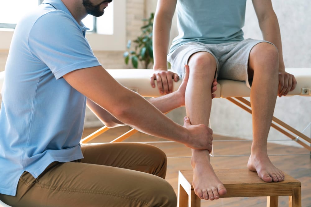physiothérapeute et chirothérapeute en train de travailler sur la jambre d'un patient assis sur une table de traitement sur la rive-sud