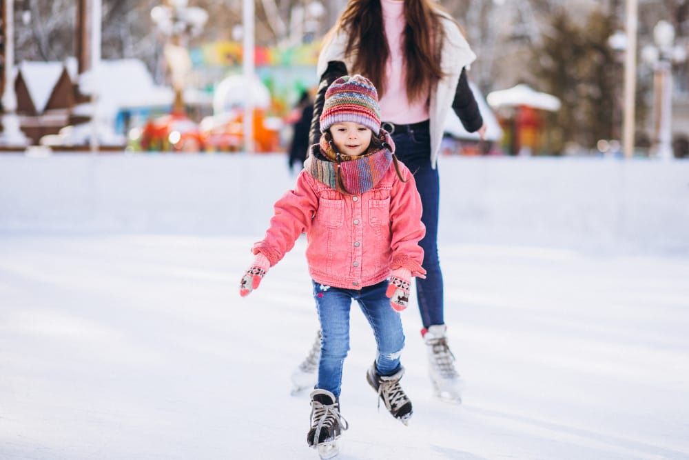 Photo d'une jeune fille et de sa mère qui patine sur un patinoire extérieur.